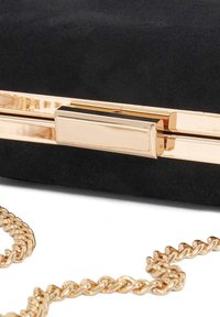 Zwarte suède clutch met een gouden sluiting en een kettingstrap. De sluiting heeft een elegante rechthoekige vorm; de strap heeft een gedraaide schakelstructuur.