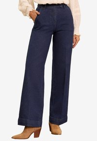 Široke traperice tamne boje s visokim strukom, s bočnim džepovima i čistim rubom. Nosit će se s svijetlom, teksturiranom majicom.