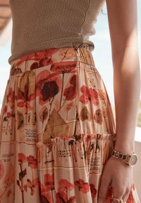 Rock mit Blumenmuster in Rottönen und Beige, mit gerafftem Bund und Rüschensaum. Dazu ein strukturierter Stricktop.