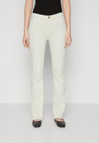 Vaqueros blancos acampanados con cinco bolsillos, trabillas para cinturón y un solo botón marrón. La tela presenta una textura suave y un acabado limpio. Se llevan zapatos planos negros.