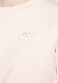 Ljusrosa sweatshirt i mjukt tyg, med en silverfärgad Nike-logotyp på bröstet; rund halsringning och raglanärmar.