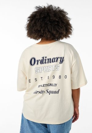 Cream-colored oversized T-shirt with short sleeves featuring navy blue text: "Ordinary Sports EST 1980 ATHLETICALLY Varsity Squad" on the back.