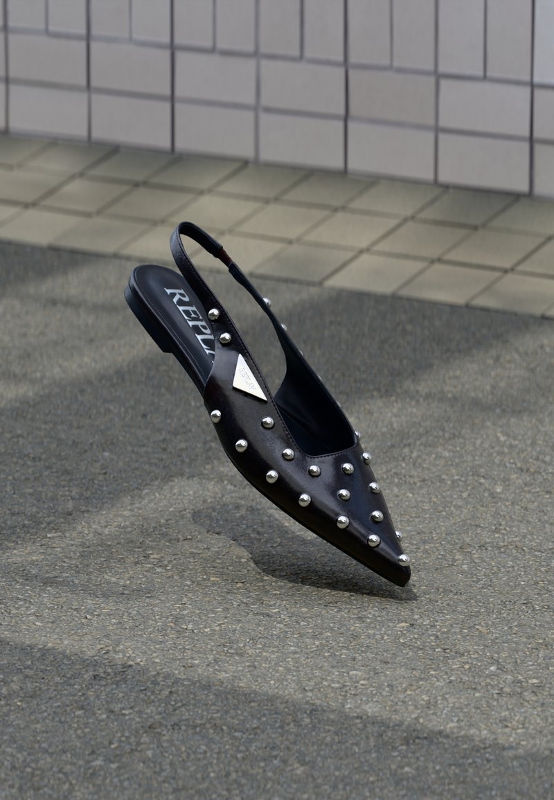Μαύρο μυτερό slingback παπούτσι από λείο υλικό, με ασημί καρφιά, επίπεδη σόλα και λογότυπο στο εσωτερικό της σόλας.