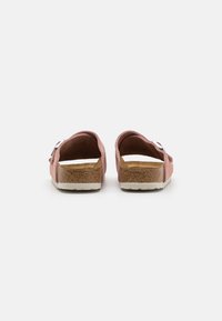 Zoccoli in pelle scamosciata rosa con apertura sul retro, soletta in sughero e suola in gomma bianca. Presentano una fibbia argentata e una texture liscia.