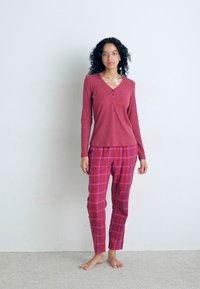 Långärmad ribbad topp i vinröd med V-ringning och knappdetalj, ihop med rutiga pyjamasbyxor i rosa och röda nyanser.