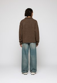Un pull en maille oversize marron avec un col, associé à un jean taille haute bleu clair et des baskets beiges, vu de l'arrière.