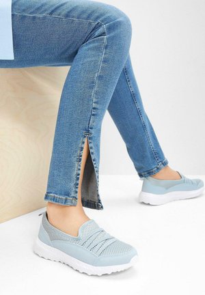 Baskets légères bleu clair à enfiler avec une tige en maille et des détails texturés, assorties à un jean en denim présentant des fentes sur les côtés à l'ourlet.
