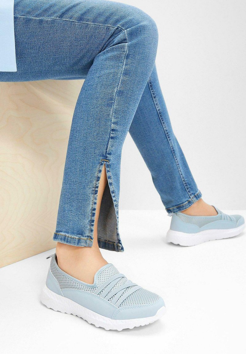Sneakers slip-on azzurri chiari con tomaia in rete e dettagli texturizzati, abbinati a jeans in denim con fessure laterali all'orlo.