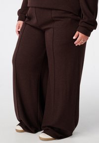 Wijdvallende broek van donkerbruine ribbelstof, met een hoge taille en subtiele verticale naden, gecombineerd met witte sneakers.