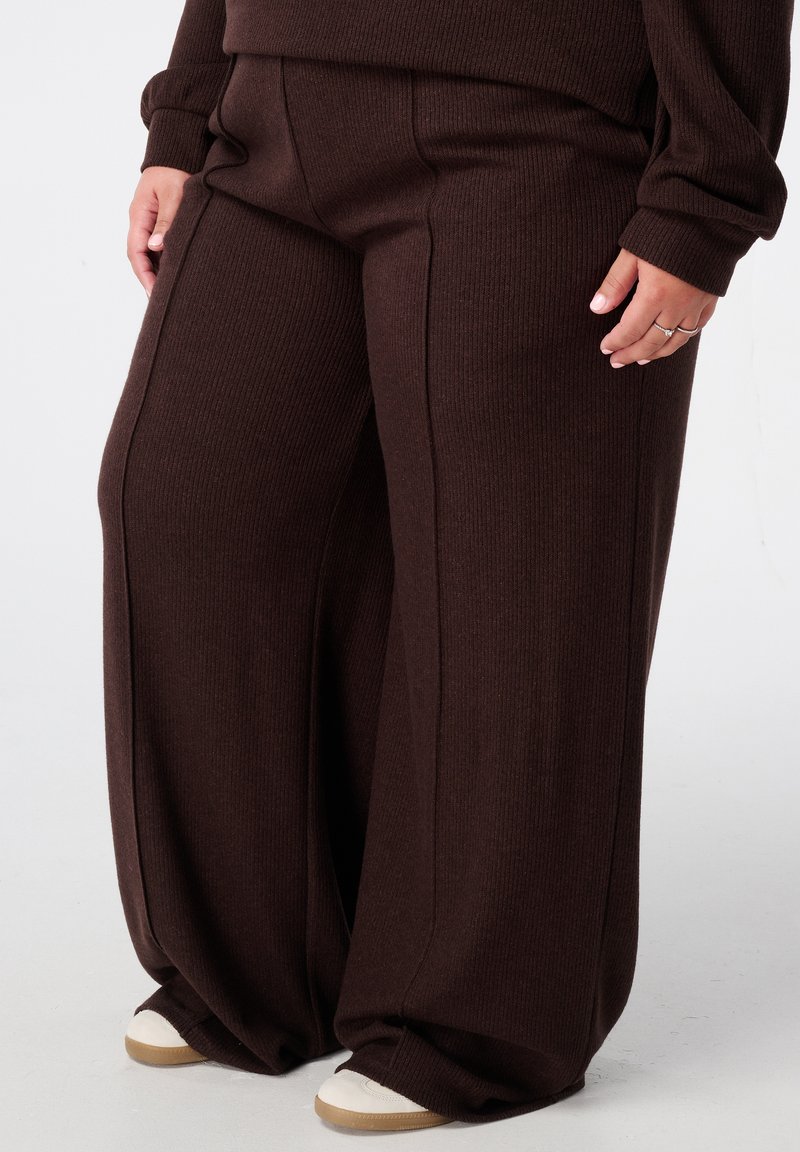 Wijdvallende broek van donkerbruine ribbelstof, met een hoge taille en subtiele verticale naden, gecombineerd met witte sneakers.
