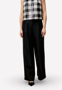 Ingeknipte zwart-wit geruite top met een getextureerde afwerking, gecombineerd met loszittende zwarte broek met omslagen en strikdetails.