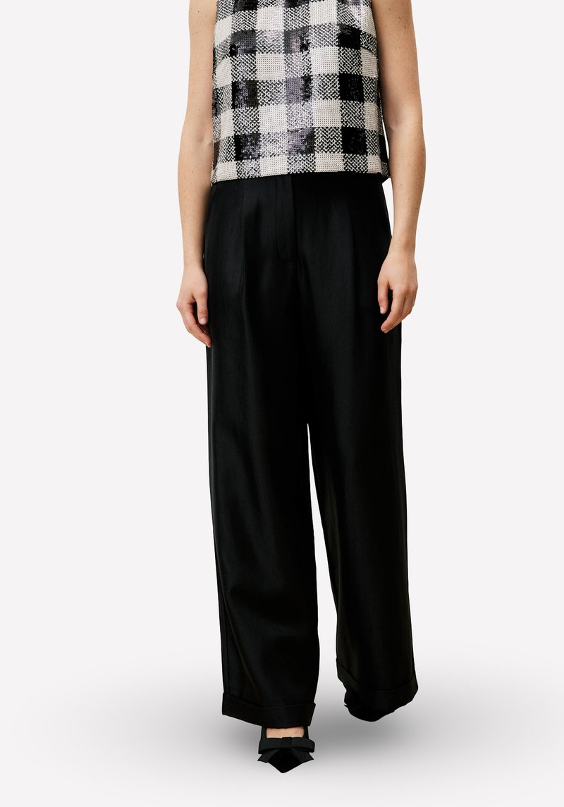 Ingeknipte zwart-wit geruite top met een getextureerde afwerking, gecombineerd met loszittende zwarte broek met omslagen en strikdetails.