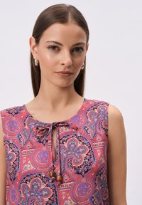 Bezrękawnik w paisley z okrągłym dekoltem, w odcieniach różu, fioletu i kremu, ozdobiony wiązaniem i drewnianymi koralikami.