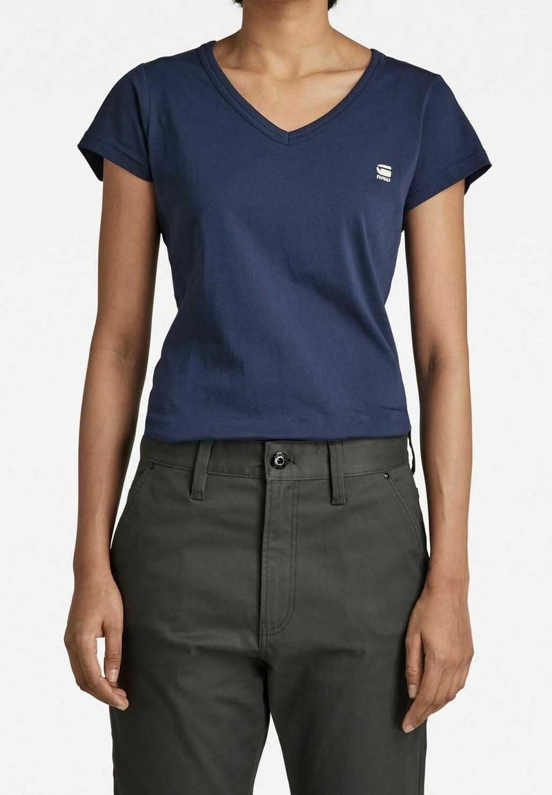 Granatowa bawełniana koszulka typu V-neck z krótkimi rękawami wykończonymi mankietami i małym logo na piersi, w zestawie z ciemnozielonymi spodniami o prostym kroju.
