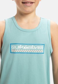 Ljusblå tanktop i bomull, med en grafisk logotyp i vitt och rosa och en rektangulär kant i blått.