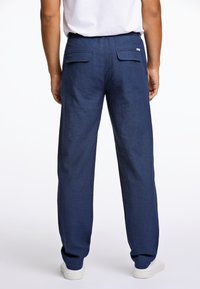 Marineblauwe linnen broek met een relaxte pasvorm, twee achterzakken en een platte tailleband, aangevuld met witte sneakers. Gestructureerde stof.