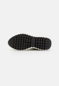 Semelle de chaussure de sport en caoutchouc noir avec un motif de bande de roulement texturé. Offre une prise durable avec une bordure blanche le long des bords. Logo de la marque visible.