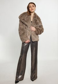 Faux fur frakke i taupe med en bred, foldet krave. Parret med skinnende, mørke metal flared bukser og sorte spidse stilettos.