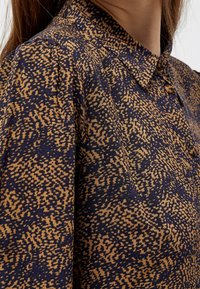 Camicia con colletto caratterizzata da un motivo a macchie blu e marroni, realizzata in tessuto testurizzato con una vestibilità comoda e dettagli dei bottoni.