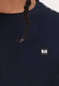 Mørkeblå bomulds T-shirt med ribbet tekstur, prydet med et firkantet sort mærke med hvid tekst, der står "WEEKEND OFFENDER."