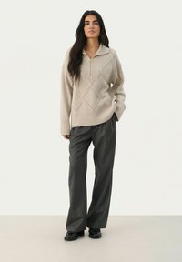 Beige knitted sweater with a half-zip collar, featuring textured diamond patterns. Paired with grey wide-leg trousers and black shoes.