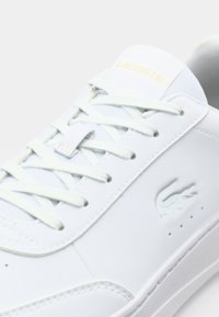 White lace-up sneaker made of smooth leather, featuring a debossed logo, minimalistic design, and accented with light-colored laces.