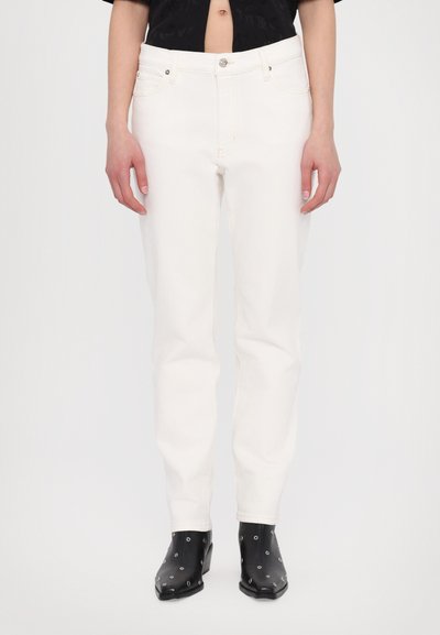 White denim jeans with a straight cut, zipper fly, and front pockets. Smooth texture and minimalist design, paired with black heeled boots.