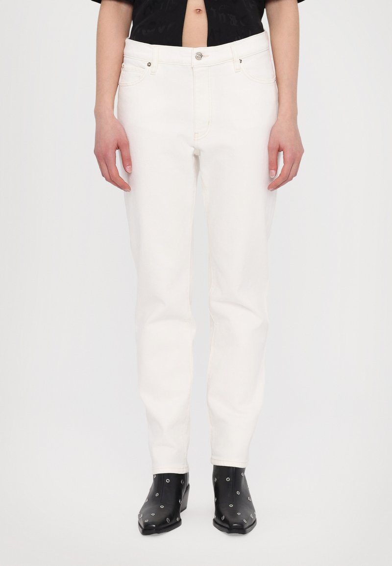 Vita denimjeans med rak skärning, blixtlås och framfickor. Slät textur och minimalistisk design, tillsammans med svarta klackstövlar.