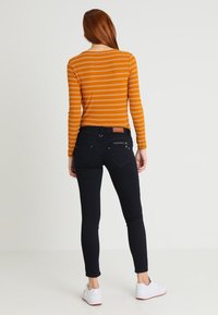 Top de manga larga a rayas naranjas combinado con jeans ajustados oscuros. Incluye bolsillos traseros, cremalleras sutiles y zapatillas blancas.