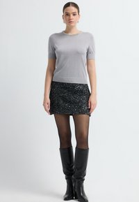 Grå kortærmet top med en prydet halsudskæring, der er parret med en sort paillet-mini nederdel og knæ-høje sorte læderstøvler. Simpelt og elegant design.