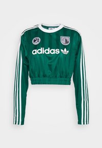 Grön kort tröja av glansigt tyg, med vita ränder på ärmarna, Adidas-logotyp och två distinkta märken på bröstet.