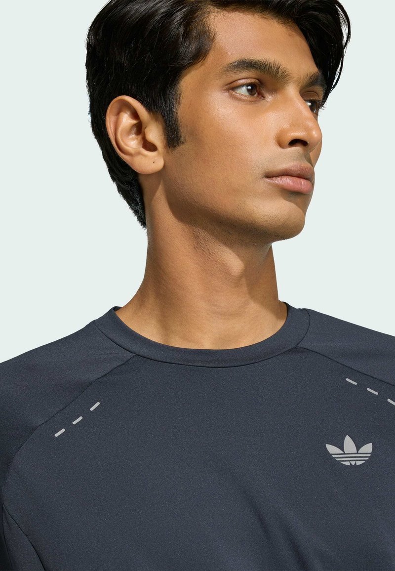 Joven con cabello corto y oscuro, vistiendo una camiseta deportiva oscura con un pequeño logo de Adidas en el pecho, mirando hacia la derecha.
