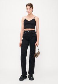 Čierny textúrovaný crop top s nastaviteľnými ramienkami, skombinovaný s vysokými čiernymi džínsami. Modelka nesie malú kabelku s leopardím vzorom. Hlavné čierne topánky.
