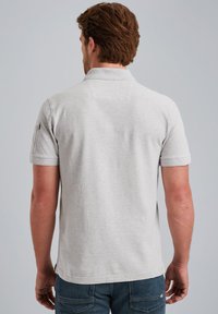 Polo shirt grigio a maniche corte con colletto, realizzato in un tessuto morbido, caratterizzato da una leggera texture e un piccolo dettaglio a slittamento sull'orlo.