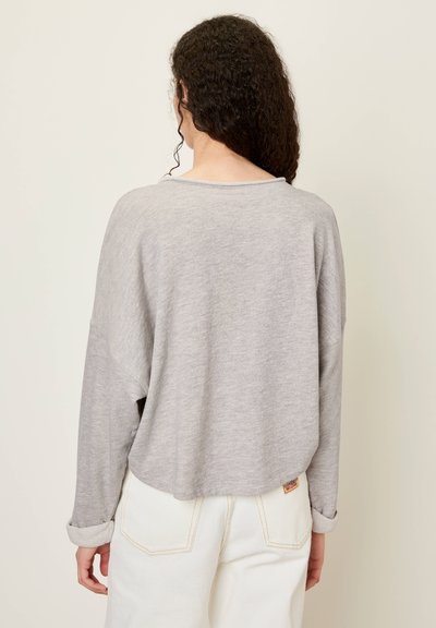 Haut gris à manches longues avec une coupe ample et un col rond, fabriqué en matériau doux. Présente des poignets retroussés et un détail d'ourlet subtil.
