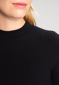 Zwart geribd hoogsluitend topje met een gestructureerde stof met verticale lijnen, die een aansluitend ontwerp en een glad oppervlak benadrukt.