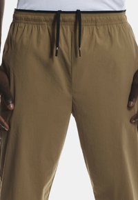 Pruunid elastsed püksid musta nööriga. Omavad sujuvat tekstuuri ja laia lõiget, on loodud mugavuse ja liikuvuse tagamiseks.