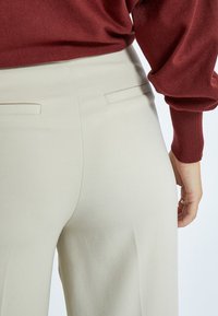 Beige široké kalhoty s hladkou texturou, se dvěma zadními kapsami a středním pasem, v kombinaci s burgundským dlouhým rukávem.