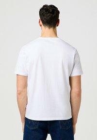 Vit bomullst-shirt med rund halsringning och korta ärmar, med enkel design och synliga sömmar vid fållen och ärmarna.