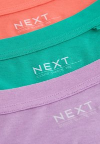 T-shirts encolure en V ample empilés, de couleurs corail, bleu sarcelle et lavande, avec des étiquettes de la marque Next visibles à l'intérieur des cols.