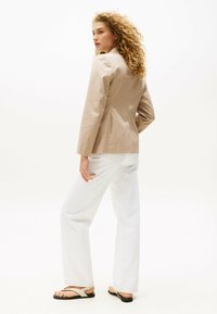 Blazer beige con maniche lunghe, forma aderente e tessuto liscio, abbinato a pantaloni bianchi a gamba larga e sandali casual.