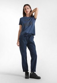 Navy blauwe katoenen T-shirt met de tekst "I AM MUSE" gedrukt in een lichtere tint, gecombineerd met bijpassende navy joggerbroeken en zwarte sneakers.