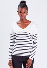 Pull en V rayé blanc et marine, avec des manches longues, une bande horizontale texturée et des accents de bouton sur l'épaule.