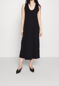 Schwarzes ärmelloses Maxikleid mit Rundhalsausschnitt, aus glattem Stoff gefertigt, mit einer lockeren Passform, die bis zur Mitte des Waden fliest.