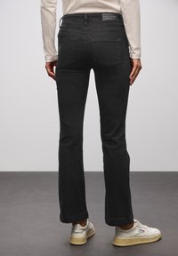 Jeans neri a zampa d'elefante realizzati in denim, con vita alta, due tasche posteriori e orlo pulito. Abbinati a sneakers di colore chiaro.