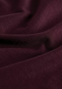 Bordowa tkanina o gładkiej, lekko teksturowanej powierzchni, delikatnie układająca się, aby pokazać głębię i miękkość. Idealna do odzieży lub tapicerki.