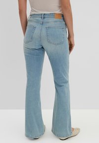 Light blue denim flared jeans with a mid-rise waist, five pockets, and a leather patch at the back. Smooth texture, casual style.