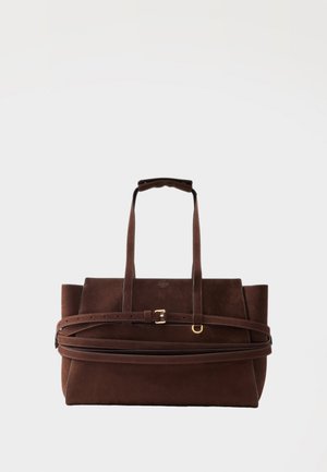 Rjava usnjena torba za na rame z dvema ročajema, nastavljivim pasom s sponko in z zlatim kovinskim obročem na enostavni svetli podlagi.