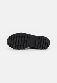 Suela de zapato de goma negra con un patrón texturizado, que presenta ranuras horizontales y verticales para tracción y estabilidad. Talla marcada como 38.