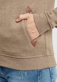Brun fleece genser med en forlomma; har en trekantet lærdetalj nær lomma. Myk tekstur og uformell design.